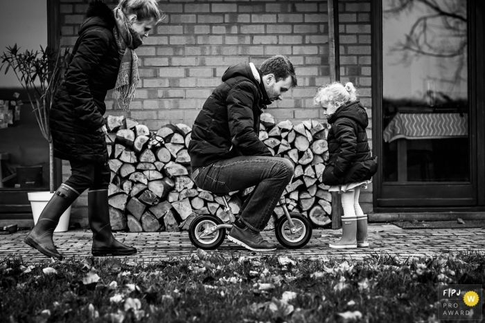 Photo by: <a href="https://www.fpja.com/documentary-family-photography-contests/emilie-marchandise/brabant-wallon/2100869">Emilie Marchandise - Belgium</a> Dad is trying to ride a small bike as his daughter watches | Belgium Family Session