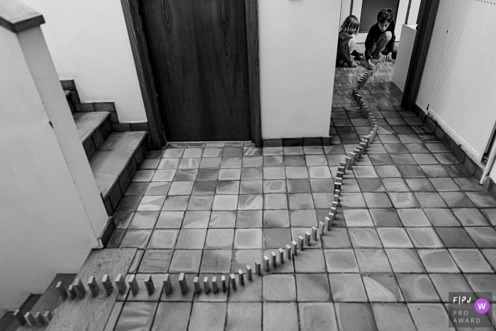 Photo by: <a href="https://www.fpja.com/documentary-family-photography-contests/emilie-marchandise/brabant-wallon/2101050">Emilie Marchandise - Belgium</a> Children line up dominos on the floor through the house | Brabant Wallon Family Photographer