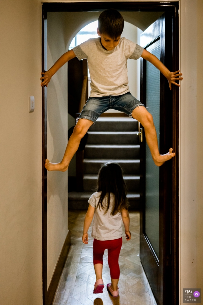 Kent	Boy climbing a doorway with girl walking under during family photo session at home in England.