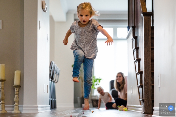 Photo by: <a href="https://www.fpja.com/documentary-family-photography-contests/viara-mileva/kingston/2101277">Viara Mileva - Canada</a> Girl jumps over hurdles in hallway during a game with family | Ontario Family Photographer