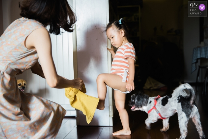 Photo by: <a href="https://www.fpja.com/documentary-family-photography-contests/leon-wong/hangzhou-city/2101301">Leon Wong - China</a> Mother puts clothes for the baby, and two dogs are also onlookers | China Photography for Families