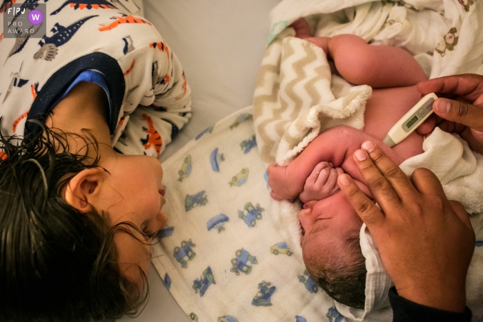 Photo by: <a href="https://www.fpja.com/documentary-family-photography-contests/adriana-costa/belo-horizonte/2101489">Adriana Costa - Brazil</a> Belo Horizonte Boy watching his newborn brother receive his first medical evaluation | Brazil family pictures