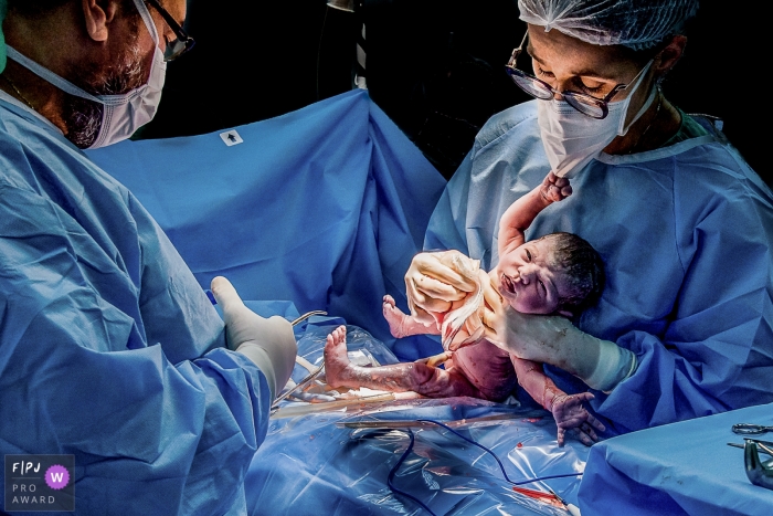 Le bébé est délivré de sa mère et tend la main pour attraper le masque du médecin | Photographie de famille à Rio de Janeiro