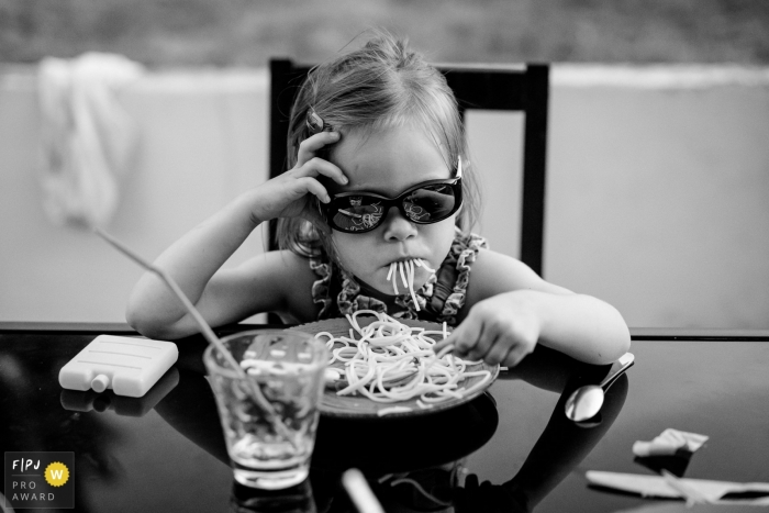 Photo by: <a href="https://www.fpja.com/documentary-family-photography-contests/sybil-rondeau/nantes/2101576">Sybil Rondeau - France</a> A little girl eat pasta with her sunglasses | France child photography
