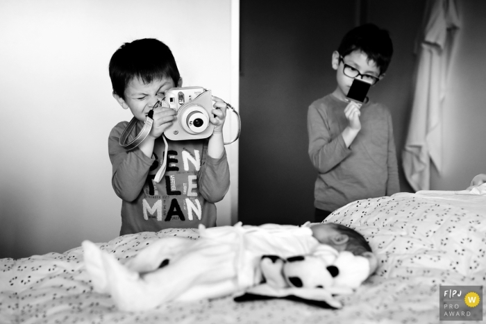 Allier family photo session with big brothers taking pictures of new baby on the bed.