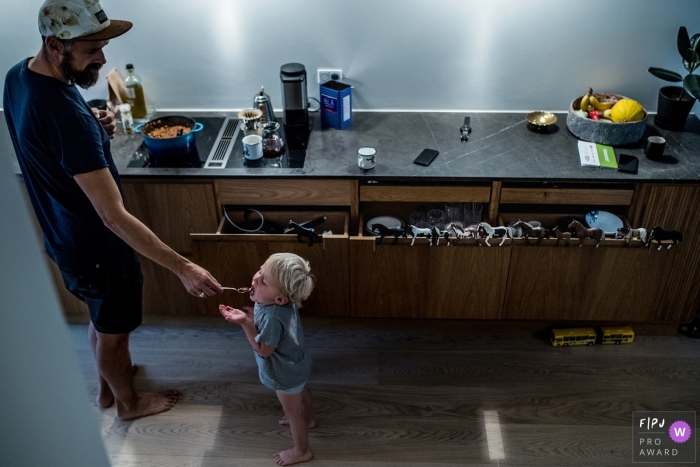 Photo by: <a href="https://www.fpja.com/documentary-family-photography-contests/frederikke-brostrup/copenhagen/2101658">Frederikke Brostrup - Denmark</a> Copenhagen daddy feeding his son a bite while he cooks dinner. Denmark family photo session in the home.