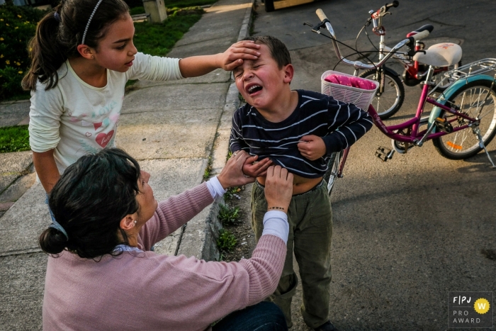 Photo by: <a href="https://www.fpja.com/documentary-family-photography-contests/alvaro-tejeda/talca/2101703">Alvaro Tejeda - Chile</a> Boy is cries to his mother and sister while in pain after what appears to be a bicycle accident | Talca Family Photographer