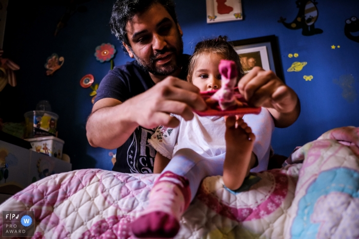 Photo by: <a href="https://www.fpja.com/documentary-family-photography-contests/alvaro-tejeda/talca/2101710">Alvaro Tejeda - Chile</a> Father helping daughter put on her socks | Talca, Chile Documentary Family Photographer