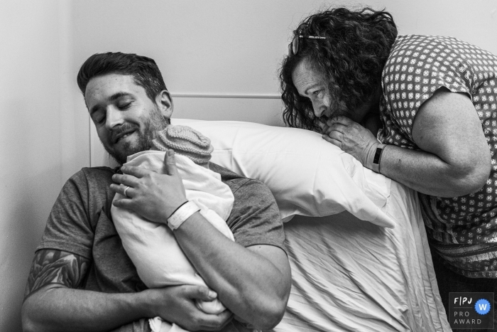 Ontario family photojournalist: Dad holds baby while grandma peers over edge of chair - birth photographer.