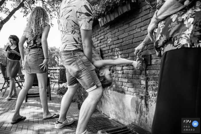 Summer time fun of a girl being held upside down while putting her hand under a water spigot | Gelderland Family Photography