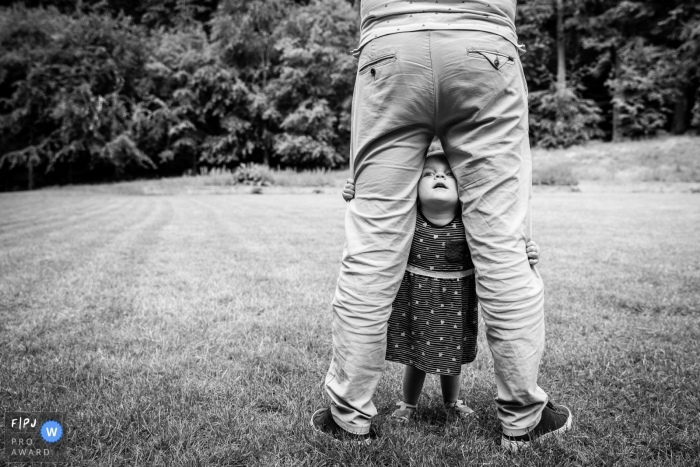 Photo by: <a href="https://www.fpja.com/documentary-family-photography-contests/angeline-dobber/gelderland/2102009">Angeline Dobber - Netherlands</a> Young girl takes a peak between dad's legs | Gelderland Family Photo