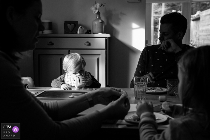 Photo by: <a href="https://www.fpja.com/documentary-family-photography-contests/angeline-dobber/gelderland/2102115">Angeline Dobber - Netherlands</a> A splash of light falls upon a young child as he take a sip at the table with family | Gelderland Family Session