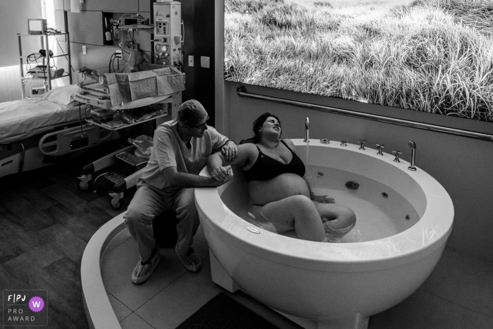 Photo by: <a href="https://www.fpja.com/documentary-family-photography-contests/liliane-cotta/rio-de-janeiro/2102181">Liliane Cotta - Brazil</a> Couple hold hands while the woman goes through labor in a bath | Brazil Birthing Photo
