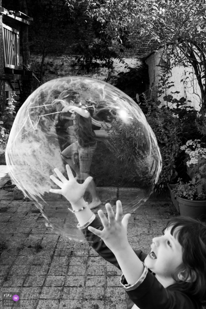 Photo by: <a href="https://www.fpja.com/documentary-family-photography-contests/ralitza-soultanova/brussels/2102256">Ralitza Soultanova - Belgium</a> The "Bubble Master" girl with an oversized bubble, playing in the backyard | Brussels Children Photography