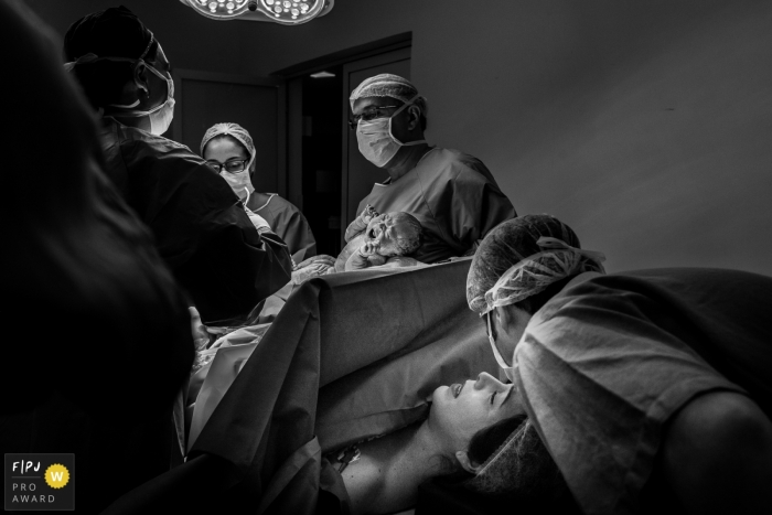 Photo by: <a href="https://www.fpja.com/documentary-family-photography-contests/ta%C3%ADs-motta/campinas/2102399">Taís Motta - Brazil</a> Hospital staff at work on a c-section while mother relaxes with the love of her husband | Sao Paulo Birthing Session