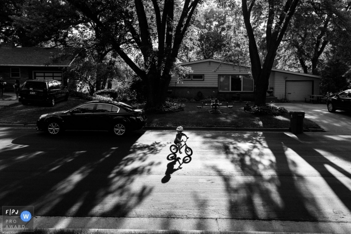 Photo by: <a href="https://www.fpja.com/documentary-family-photography-contests/jen-lucas/madison/2102601">Jen Lucas - United States</a> Wisconsin family photography | Child rides his bike in street on a summer's day.