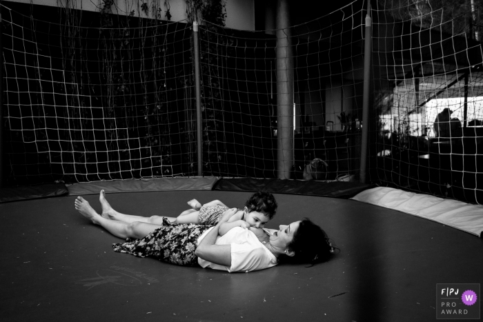 Photo by: <a href="https://www.fpja.com/documentary-family-photography-contests/joni-pereira/florianopolis/2102658">Joni Pereira - Brazil</a> Mother breastfeeds baby on trampoline at home | Santa Catarina family photography