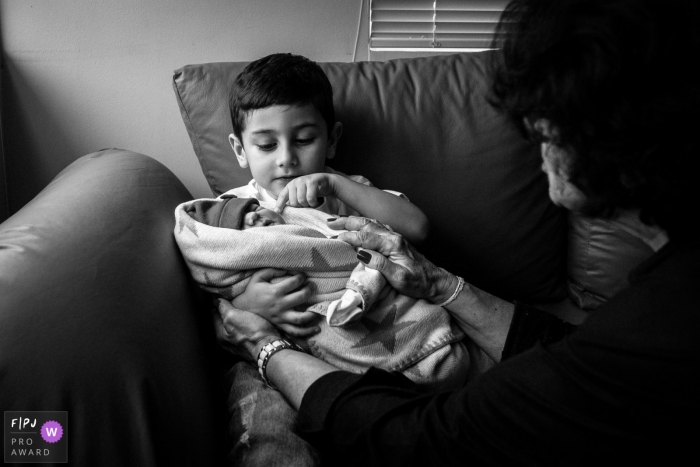 Photo by: <a href="https://www.fpja.com/documentary-family-photography-contests/joni-pereira/florianopolis/2102663">Joni Pereira - Brazil</a> Boy looks over the details of his new sister while sitting on a sofa | Brazil newborn photography