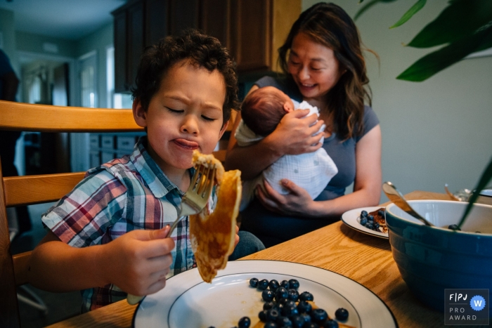 Madison Wisconsin Family Photographer | Big brother makes a face at his pancake while Mom smiles at newborn.