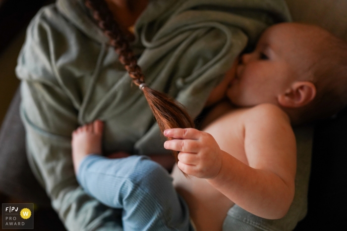 Photo by: <a href="https://www.fpja.com/documentary-family-photography-contests/ron-storer/seattle/2102748">Ron Storer - United States</a> Child breastfeeding and holding onto mom's hair | Seattle, Washington mother and child photography