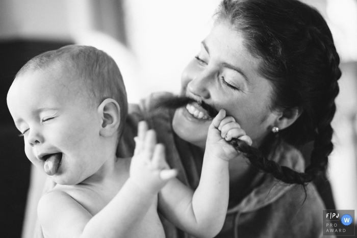 Photo by: <a href="https://www.fpja.com/documentary-family-photography-contests/ron-storer/seattle/2102749">Ron Storer - United States</a> A baby makes a face while holding onto his mom's hair | Washington Family and Child Photography