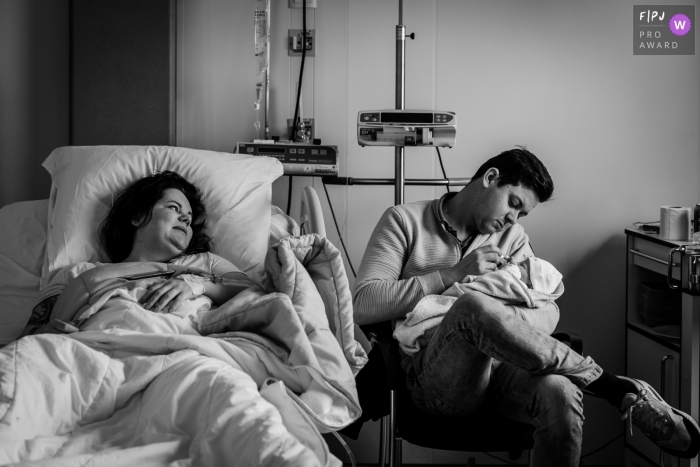 Photo by: <a href="https://www.fpja.com/documentary-family-photography-contests/marjolein-roossien/groningen/2104237">Marjolein Roossien - Netherlands</a> Father feeding his new baby as mom looks on after the birth of their child at Martini Ziekenhuis
