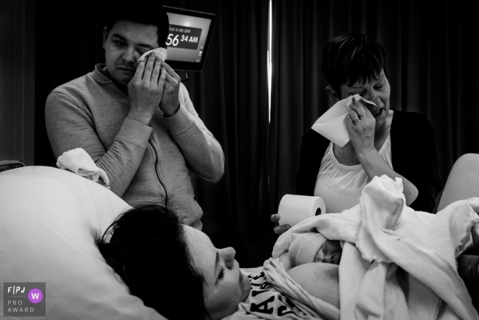 Photo by: <a href="https://www.fpja.com/documentary-family-photography-contests/marjolein-roossien/groningen/2104238">Marjolein Roossien - Netherlands</a> Martini Ziekenhuis birthing image of new mom with baby as father and family member are having tears of joy.