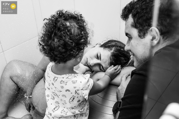 Photo by: <a href="https://www.fpja.com/documentary-family-photography-contests/gisele-soares/rio-de-janeiro/2104570">Gisele Soares - Brazil</a> In Rio de Janeiro Brazil During labor, the pregnant woman receives the affection of her eldest daughter, beside her father