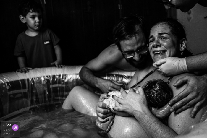 La mère est ravie de joie après avoir donné naissance à un nouveau bébé, alors que son jeune fils regarde et que son père regarde son nouveau fils.