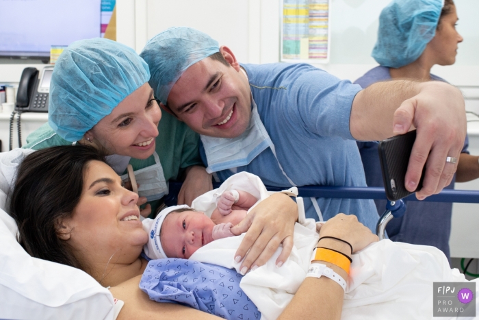 Photo by: <a href="https://www.fpja.com/documentary-family-photography-contests/cibele-piovesan/sao-paulo/2104777">Cibele Piovesan - Brazil</a> Sao Paulo family together after the birth of their baby taking a selfie in the operating room at Hospital Albert Einstein