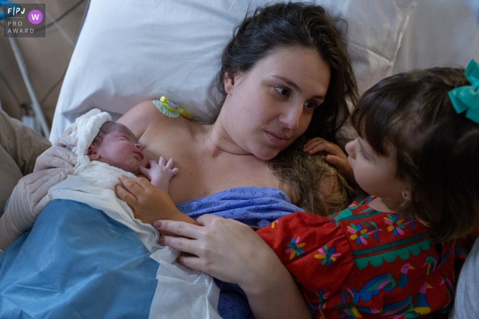 Photo by: <a href="https://www.fpja.com/documentary-family-photography-contests/cibele-piovesan/sao-paulo/2104784">Cibele Piovesan - Brazil</a> Sao Paulo Brazil mom holds her baby in the hospital as her daughter looks on at Hospital Albert Einstein