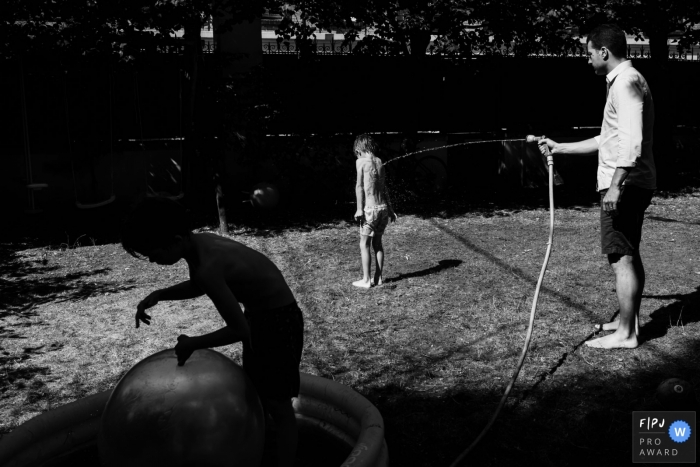 Photo by: <a href="http://fpja.com/documentary-family-photography-contests/annie-gozard/paris/2102927">Annie Gozard - France</a> A father spraying his son with water in the backyard during a France family shoot.