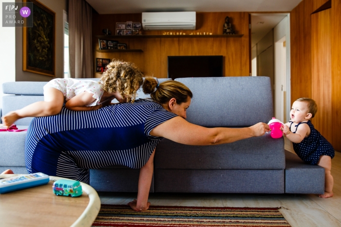 Photo by: <a href="https://www.fpja.com/documentary-family-photography-contests/graziela-ventura/sao-paulo/2102969">Graziela Ventura - Brazil</a> Sao Paulo mother reaching to her toddler on hands and knees as a young child takes a ride on her back.