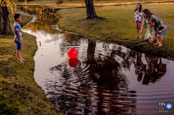 La famille Minas Gerais joue avec une grosse balle rouge tombée dans un ruisseau difficile à atteindre depuis le bord de l'eau.