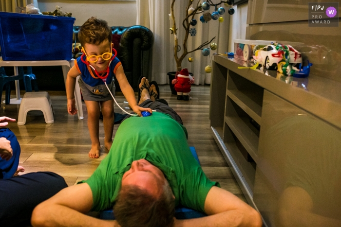 Photo by: <a href="https://www.fpja.com/documentary-family-photography-contests/adriana-costa/belo-horizonte/2103449">Adriana Costa - Brazil</a> Belo Horizonte Minas Gerais boy plays being a doctor examining his father