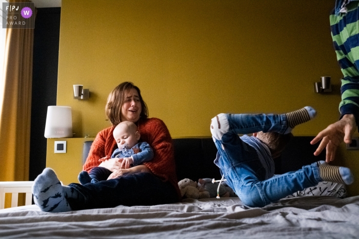 Une famille flamande avec maman et enfants assis sur un lit.