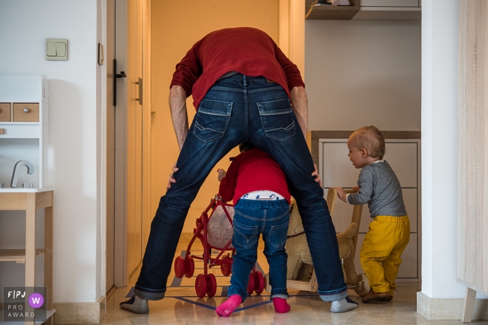 Une petite fille et son père habillés dans les mêmes couleurs avec un jeune enfant à leurs côtés jouent avec des poussettes jouets.