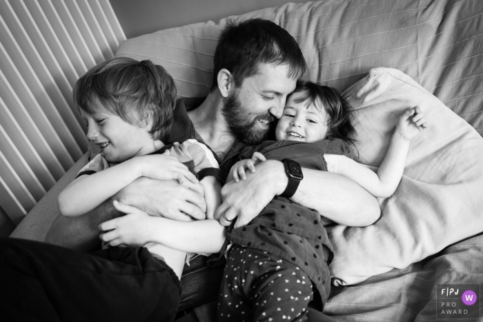 Photo by: <a href="https://www.fpja.com/documentary-family-photography-contests/alice-chapman/cambridgeshire/2104044">Alice Chapman - United Kingdom</a> England family photo shoot of a dad cuddling with his children