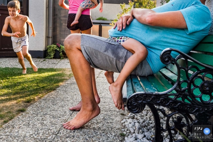 Photo by: <a href="https://www.fpja.com/documentary-family-photography-contests/katrin-k%C3%BCllenberg/dusseldorf/2104220">Katrin Küllenberg - Germany</a> Dusseldorf North Rhine-Westphalia child Hiding under dad on the bench