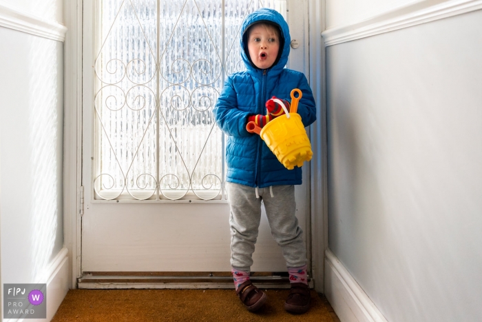 Photo by: <a href="https://www.fpja.com/documentary-family-photography-contests/linda-mauch/kent/2104295">Linda Mauch - United Kingdom</a> Kent England Little girl waits by the door in big winter coat holding bucket and spade