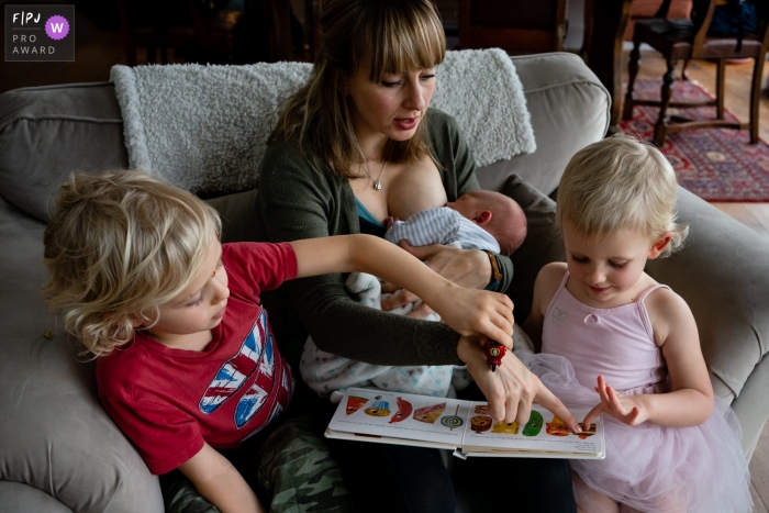 Kent	England Nursing mother and daughter read a book while big brother plays cars on mum