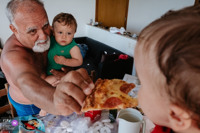 Photo by: <a href="https://www.fpja.com/documentary-family-photography-contests/thiago-braga/florianopolis/2104793">Thiago Braga - Brazil</a> Florianopolis Santa Catarina man feeding a child pizza