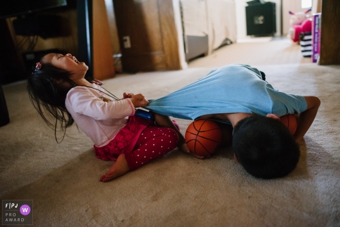 Photo by: <a href="https://www.fpja.com/documentary-family-photography-contests/tiffany-luong/los-angeles/2104872">Tiffany Luong - United States</a> Los Angeles siblings fight and yell as they play with basketballs on the livingroom floor