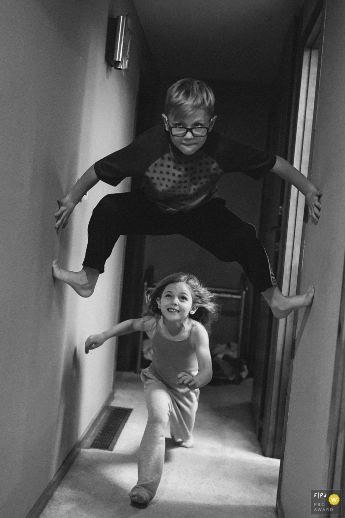 Photo by: <a href="https://www.fpja.com/documentary-family-photography-contests/ron-storer/seattle/2104878">Ron Storer - United States</a> Seattle Family Photo of a girl running under boys legs in hallway