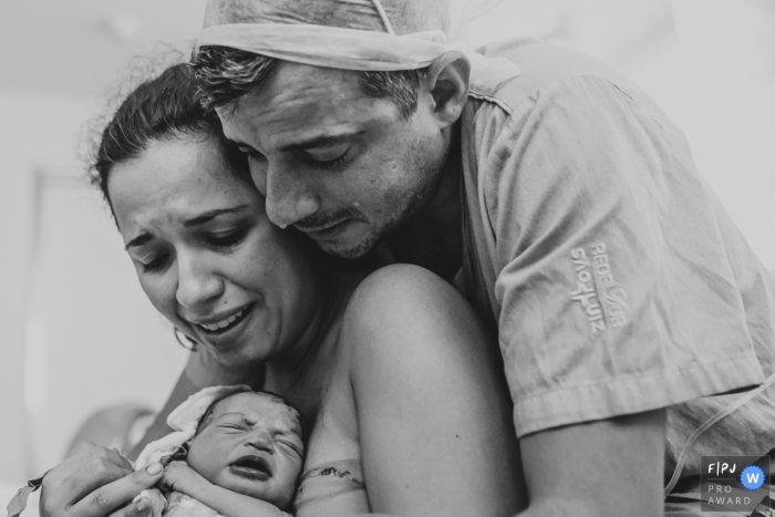 Photo by: <a href="https://www.fpja.com/documentary-family-photography-contests/ellen-brito/sao-paulo/2105176">Ellen Brito - Brazil</a> Sao Paulo Brazil hospital birth image of mom, dad and new baby.