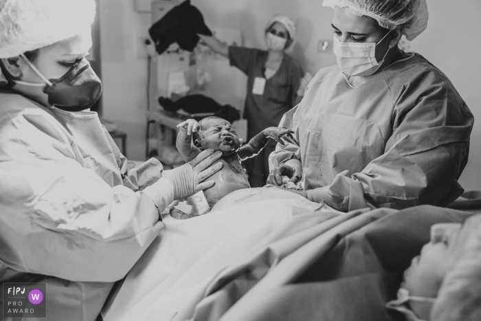 Photo by: <a href="https://www.fpja.com/documentary-family-photography-contests/ellen-brito/sao-paulo/2105199">Ellen Brito - Brazil</a> Hospital e Maternidade São Luiz birthing image of baby emerging from his mother as the mom leans up to take a peek.