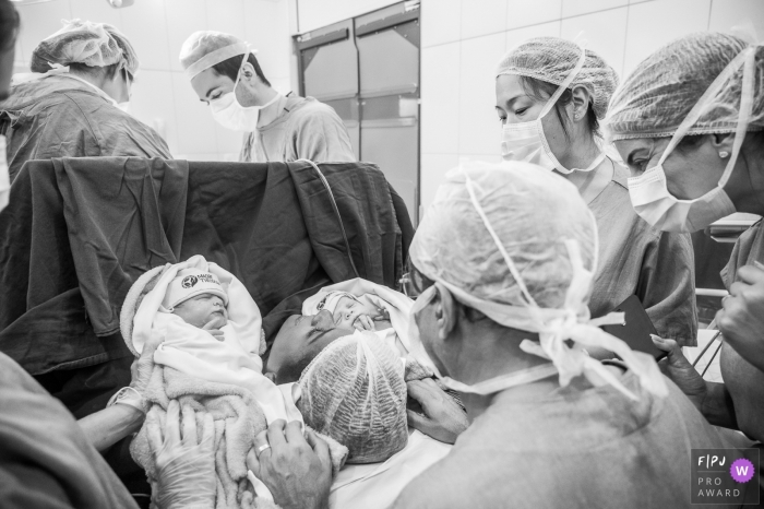 Photo by: <a href="https://www.fpja.com/documentary-family-photography-contests/ta%C3%ADs-motta/campinas/2106352">Taís Motta - Brazil</a> Hospital Madre Theodora image of mom meeting baby as the medical team work on mom in the background | Sao Paul family photo