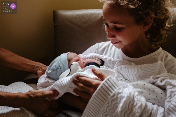 Photo by: <a href="https://www.fpja.com/documentary-family-photography-contests/thiago-braga/florianopolis/2106569">Thiago Braga - Brazil</a> Image capturing a young lady receiving her newborn cousin in her lap for the first time from her grandmother at the Ilha Hospital e Maternidade