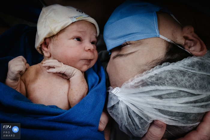 Photo by: <a href="https://www.fpja.com/documentary-family-photography-contests/thiago-braga/florianopolis/2106579">Thiago Braga - Brazil</a> Mother in a mask being introduced to her new baby after giving birth at the Maternidade Santa Helena in Brazil