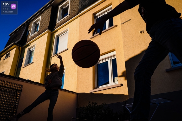 Silhouette of children playing basketball with a brightly sunlit building behind them | Germany kid sports photography